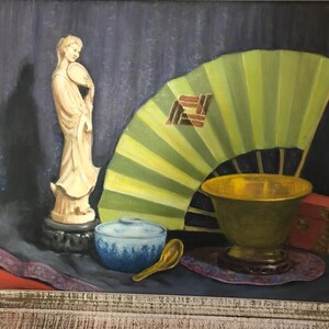 May include: A still life painting featuring a white porcelain figurine, a green folding fan, a gold bowl, a blue and white bowl, and a wooden box. The painting is framed in a light wood frame.