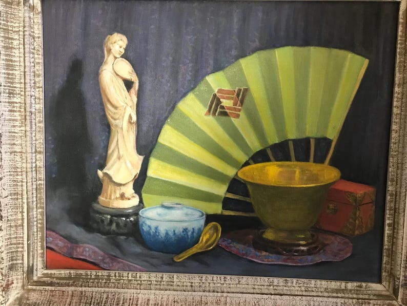 May include: A still life painting featuring a white porcelain figurine, a green folding fan, a gold bowl, a blue and white bowl, and a wooden box. The painting is framed in a light wood frame.
