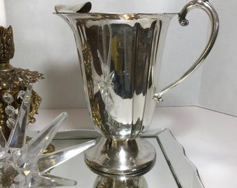 May include: A silver pitcher with a fluted design and a handle. The pitcher is sitting on a mirrored tray.
