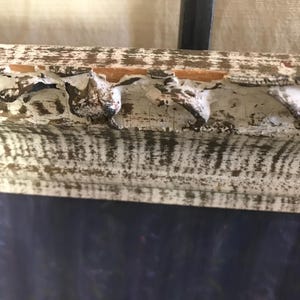 May include: A white wooden frame with a distressed finish. The frame has a decorative edge with a series of small, rounded protrusions. The frame is partially obscured by a dark blue background.