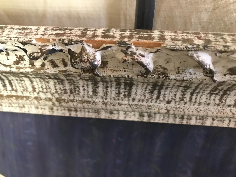 May include: A white wooden frame with a distressed finish. The frame has a decorative edge with a series of small, rounded protrusions. The frame is partially obscured by a dark blue background.