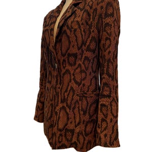 May include: A brown and black snakeskin-patterned blazer. The blazer has a notched lapel, a two-button closure, and a single pocket. The jacket is displayed on a mannequin.