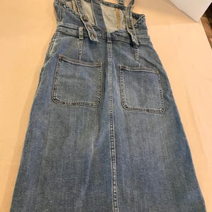 Peut inclure: Une robe en jean bleu avec des bretelles r&eacute;glables et deux grandes poches sur le devant.