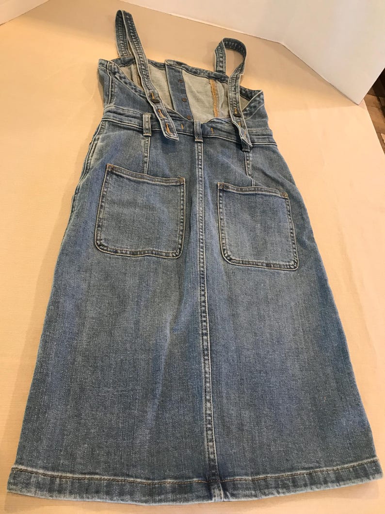 Peut inclure: Une robe en jean bleu avec des bretelles r&eacute;glables et deux grandes poches sur le devant.