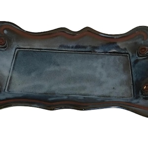 May include: A rectangular ceramic tray with a dark blue glaze and brown accents. The tray has curved handles and a decorative border. The overall shape is rectangular, with a slightly scalloped edge.