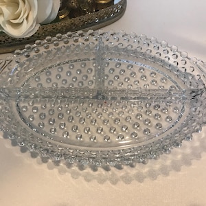 Może przedstawiać: Przezroczysta szklana tacka do serwowania z podzielonym środkiem i perłowym obrzeżem. Taca ma owalny kształt i fakturowaną powierzchnię.