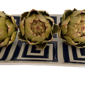 May include: A rectangular decorative tray with a geometric pattern in navy blue and cream, holding three artichoke-shaped decorative objects. The artichokes are green with reddish-brown tips.