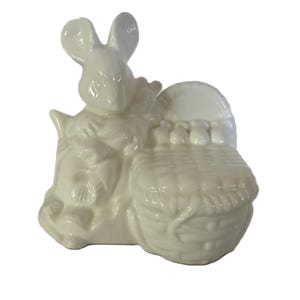 Puede incluir: Figura de conejo de Pascua de cerámica color crema con una cesta. El conejo está sentado junto a una cesta tejida. La figura es un artículo decorativo, perfecto para Pascua.