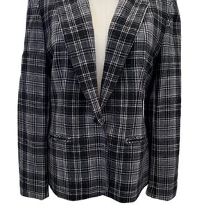 May include: A black, white, and gray plaid blazer with a notched lapel and two front pockets. The blazer is displayed on a white mannequin and has a single-button closure. The pattern is a classic, timeless design.