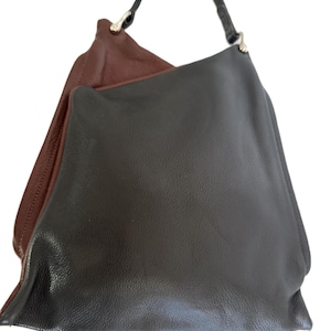Puede incluir: Un bolso de hombro de cuero de dos tonos. El exterior es marr&oacute;n oscuro, mientras que el interior es marr&oacute;n claro. El bolso tiene una sola correa negra y herrajes plateados.