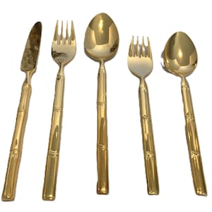 May include: A set of five gold-colored bamboo-style flatware pieces. The set includes a knife, two forks, and two spoons. The utensils have a shiny finish and are arranged against a white background.