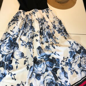 May include: A black sleeveless dress with a white skirt patterned with blue flowers. A straw sun hat sits beside the dress. The skirt has a black and red striped border.