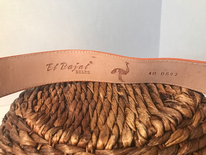 Op de afbeelding: Close-up van een bruine leren riem met de tekst "El Dajal Belts" en een struisvogelontwerp. De riem heeft ook de nummers "40 0892" erop gedrukt.