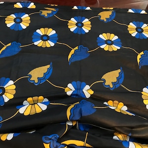 以下が含まれることがあります： 黄色、白、青のスタイリッシュな花が繰り返しパターンで描かれた黒い布。花は中央に円があり、細い黄色の線でつながっています。