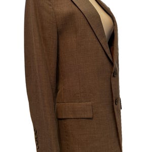 Puede incluir: Blazer marrón con un sutil patrón de rayas finas. El blazer presenta solapas con muescas, un bolsillo en el pecho y dos bolsillos delanteros. Las mangas tienen tres botones. El blazer se muestra en un maniquí.