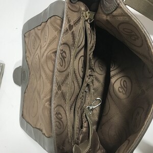 Puede incluir: El interior de un bolso de mano de cuero marr&oacute;n con un bolsillo con cremallera y un forro estampado en marr&oacute;n y blanco. El forro presenta un logotipo repetido de una letra estilizada "G" dentro de un coraz&oacute;n.