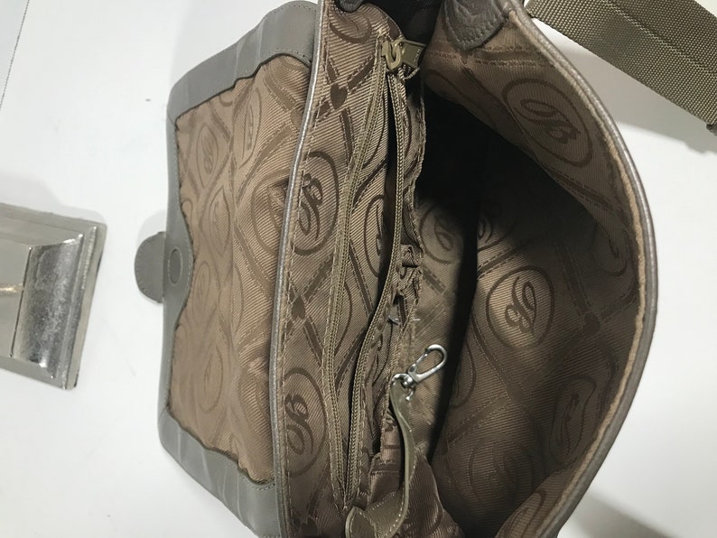 Puede incluir: El interior de un bolso de mano de cuero marr&oacute;n con un bolsillo con cremallera y un forro estampado en marr&oacute;n y blanco. El forro presenta un logotipo repetido de una letra estilizada "G" dentro de un coraz&oacute;n.