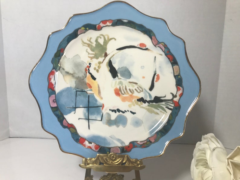 May include: A blue and white ceramic plate with a watercolour design of a bird and flowers. The plate has a scalloped edge and a gold rim.