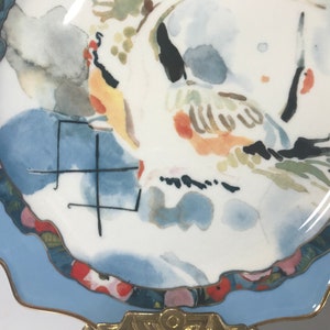 May include: A white ceramic plate with a blue rim and a watercolour design of birds and flowers. The plate has a gold trim and a scalloped edge.