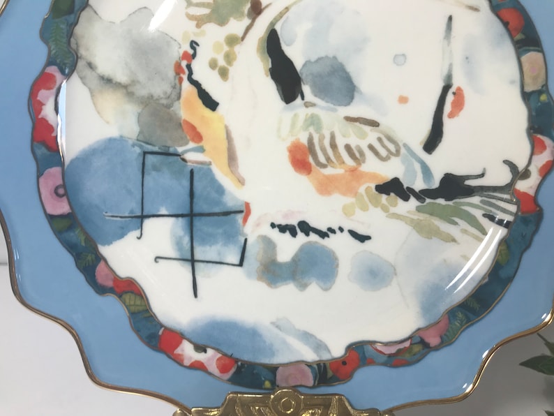 May include: A white ceramic plate with a blue rim and a watercolour design of birds and flowers. The plate has a gold trim and a scalloped edge.