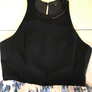 May include: A black sleeveless dress with a beaded neckline and a floral print skirt. The skirt has a white background with blue floral patterns. The dress features a high neckline and a fitted bodice.