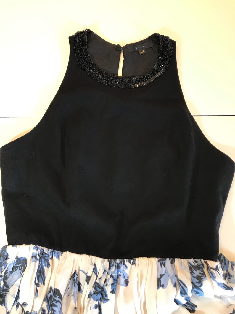 May include: A black sleeveless dress with a beaded neckline and a floral print skirt. The skirt has a white background with blue floral patterns. The dress features a high neckline and a fitted bodice.