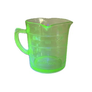 May include: A transparent, neon green measuring cup with a handle and a pouring spout. The cup has markings for measurements, including "ONE CUP". The cup is made of glass and is set against a white background.