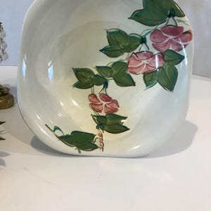 May include: A white ceramic bowl with a floral design. The bowl has a square shape with rounded corners and features a hand-painted design of pink flowers and green leaves.