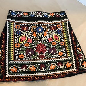 Puede incluir: Una falda negra con un patr&oacute;n de bordado floral colorido. La falda tiene un dobladillo festoneado y una cintura con un dise&ntilde;o floral.