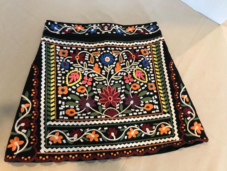 Puede incluir: Una falda negra con un patr&oacute;n de bordado floral colorido. La falda tiene un dobladillo festoneado y una cintura con un dise&ntilde;o floral.