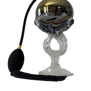 May include: A vintage perfume atomizer with a gold-toned spherical top and a clear glass base. The atomizer has a black bulb and a matching tassel. The glass base features an intricate, swirling design.
