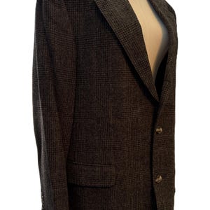 Peut inclure: Un blazer gris foncé avec un motif à carreaux subtil. La veste a un revers cranté, deux boutons sur le devant et une poche poitrine unique. Le blazer est présenté sur un mannequin.