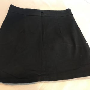 Puede incluir: Una falda mini negra de dise&ntilde;o sencillo. La falda tiene una cremallera en la parte posterior y un dobladillo recto.