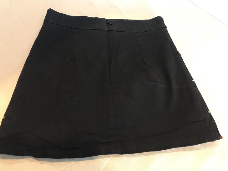 Puede incluir: Una falda mini negra de dise&ntilde;o sencillo. La falda tiene una cremallera en la parte posterior y un dobladillo recto.