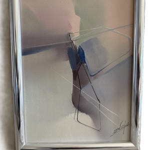 Op de afbeelding: Abstract schilderij in een zilveren lijst. Het kunstwerk toont zachte pastelkleuren, waaronder roze, blauw en grijs, met geometrische vormen en lijnen. Het schilderij is rechtsonder gesigneerd.