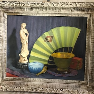 May include: A still life painting of a white porcelain figurine, a green and yellow fan, a blue and white bowl, a gold bowl, and a red box. The painting is framed in a white wooden frame.