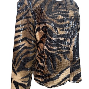 Op de afbeelding: Een bruin en zwart imitatie leren jasje met een reptielenpatroon. De jas heeft een ronde hals, lange mouwen en drie zwarte knopen aan de voorkant. Het patroon van de jas lijkt op tijgerstrepen.