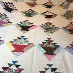 May include: A white quilt with a patchwork design featuring a variety of colors and patterns. The quilt is made up of squares and triangles, and each square features a different design. The quilt is a beautiful example of traditional quilting.