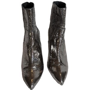 May include: A pair of metallic silver ankle boots with pointed toes. The boots have a textured, crinkled appearance and a small heel. The boots are displayed against a white background.