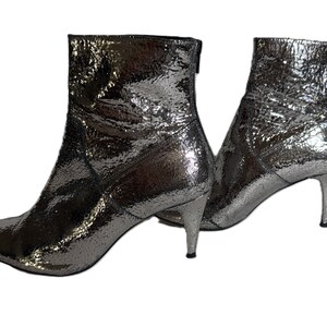 May include: Silver ankle boots with pointed toes and stiletto heels. The boots have a textured, metallic finish and a zip at the back. The boots are set against a white background.