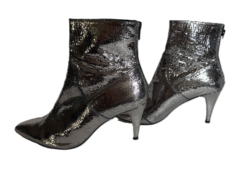 May include: Silver ankle boots with pointed toes and stiletto heels. The boots have a textured, metallic finish and a zip at the back. The boots are set against a white background.