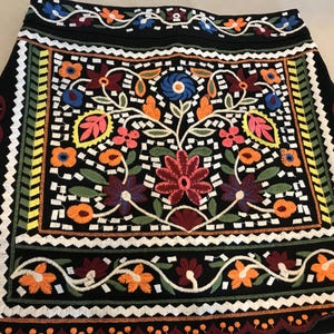 Puede incluir: Una minifalda negra con bordado floral de colores. La falda tiene un patr&oacute;n geom&eacute;trico alrededor del borde.