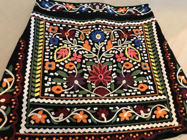 Puede incluir: Una minifalda negra con bordado floral de colores. La falda tiene un patr&oacute;n geom&eacute;trico alrededor del borde.