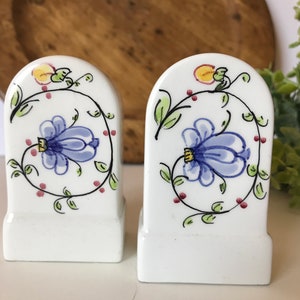 May include: A pair of white ceramic salt and pepper shakers with a blue and green floral design. The shakers are shaped like small arches.