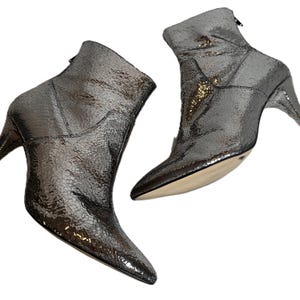 May include: Metallic silver ankle boots with pointed toes and stiletto heels. The boots feature a textured, reptile-like pattern and a back zipper. The heels are approximately 7.6 cm high.
