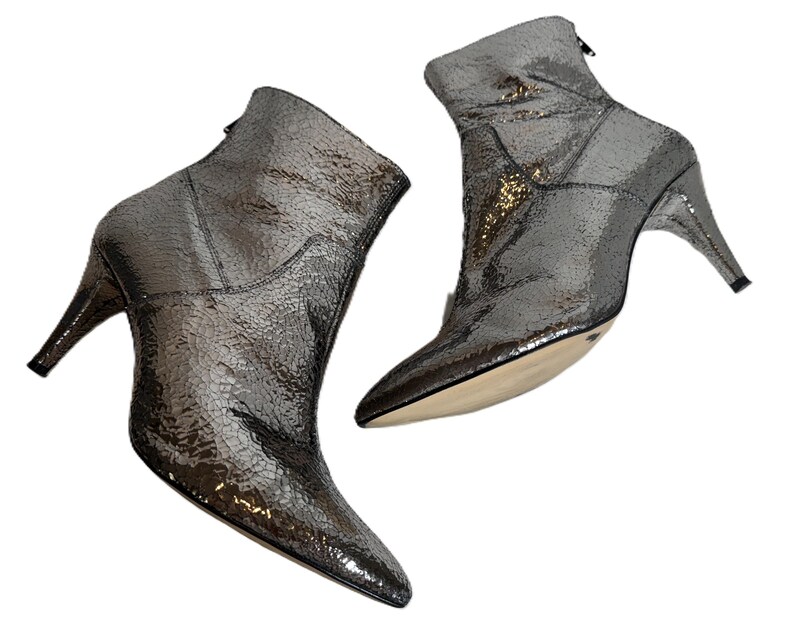 May include: Metallic silver ankle boots with pointed toes and stiletto heels. The boots feature a textured, reptile-like pattern and a back zipper. The heels are approximately 7.6 cm high.