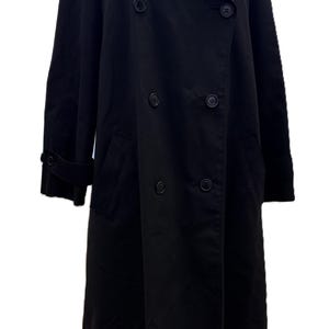 May include: A black trench coat with a double-breasted design. The coat features a wide collar, button closures, and a long length. The sleeves have buttoned cuffs, and there are pockets on the front. The coat is made of a smooth, solid black fabric.