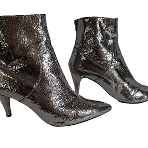 May include: Silver ankle boots with a textured, metallic finish. The boots have pointed toes, a small heel, and a back zipper. The heels are approximately 6.35 cm high.