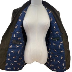 Puede incluir: Un blazer verde oscuro con forro azul estampado con ilustraciones de perros. El blazer tiene dos bolsillos y la etiqueta Macy's men's store es visible. La etiqueta Lauren también es visible.
