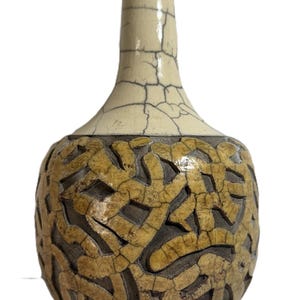 May include: A decorative ceramic vase with a unique design. The vase features a cream-colored neck and a bulbous body with a textured, interwoven pattern in shades of brown and tan. The surface has a crackled effect.